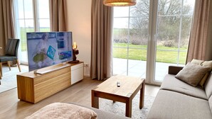 A modern living room with a television, sofa, coffee table, and a view of a garden through large windows.