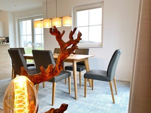 Un espace repas avec une table et des chaises en bois, un grand tronc d’arbre décoratif servant de centre de table, et un luminaire suspendu.