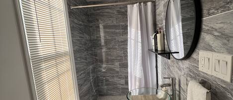 Une salle de bain moderne avec un lavabo en verre en forme de bol, un miroir et un rideau de douche.