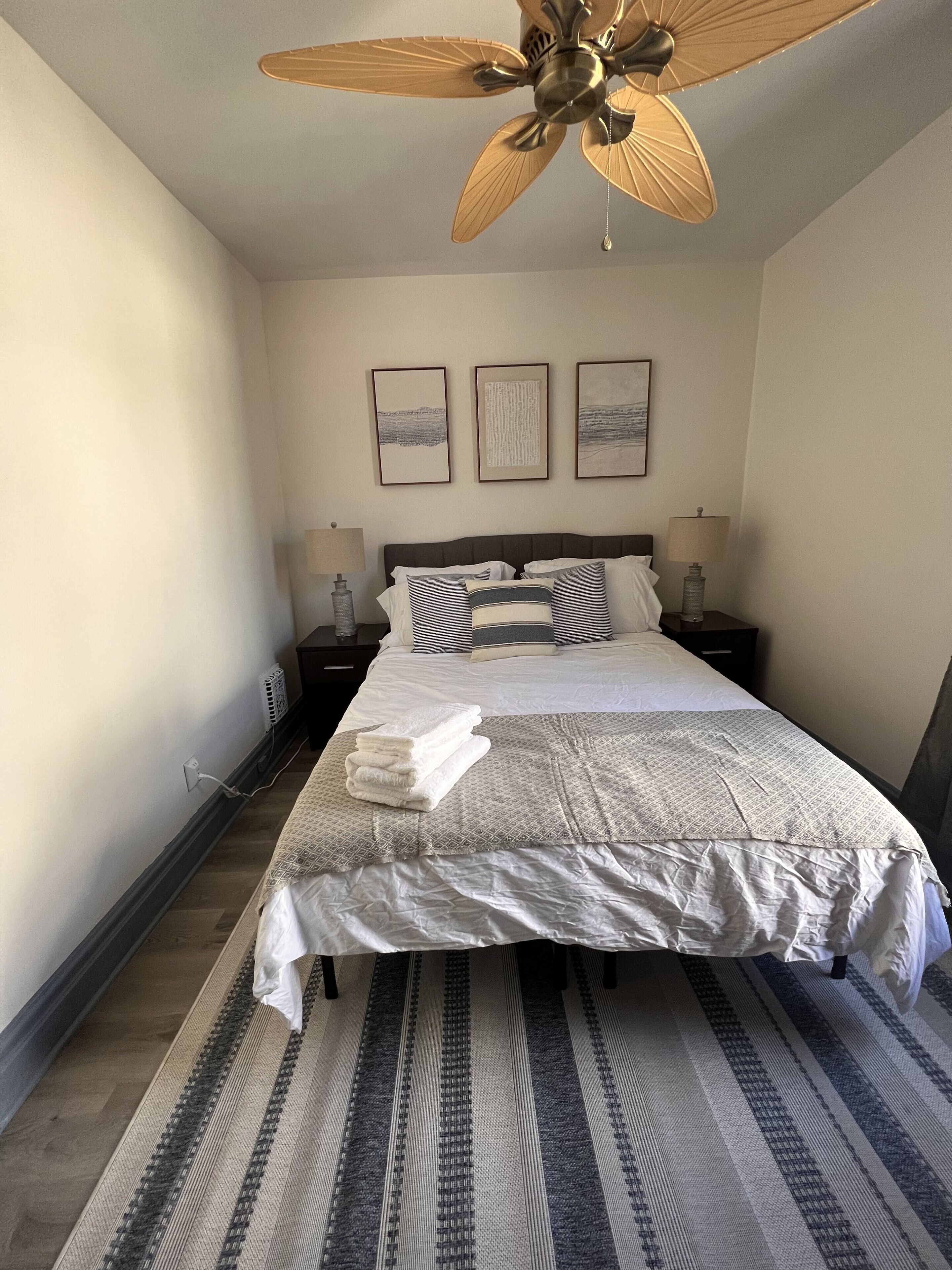 A neatly made bed with a patterned bedspread, two bedside lamps, and a ceiling fan.