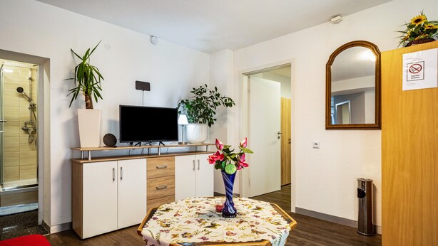 Et moderne værelse med fjernsyn, et træskab, et spejl og et bord med blomstret dug.