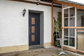 A house with a dark door, a small table, and a window with a wooden frame.