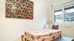 A room with a table covered in a floral tablecloth, a wall-mounted artwork, a window with blinds, and a radiator. - Holiday Apartment 'Nguyen Und Le 2' with Wi-Fi (Neukirch)