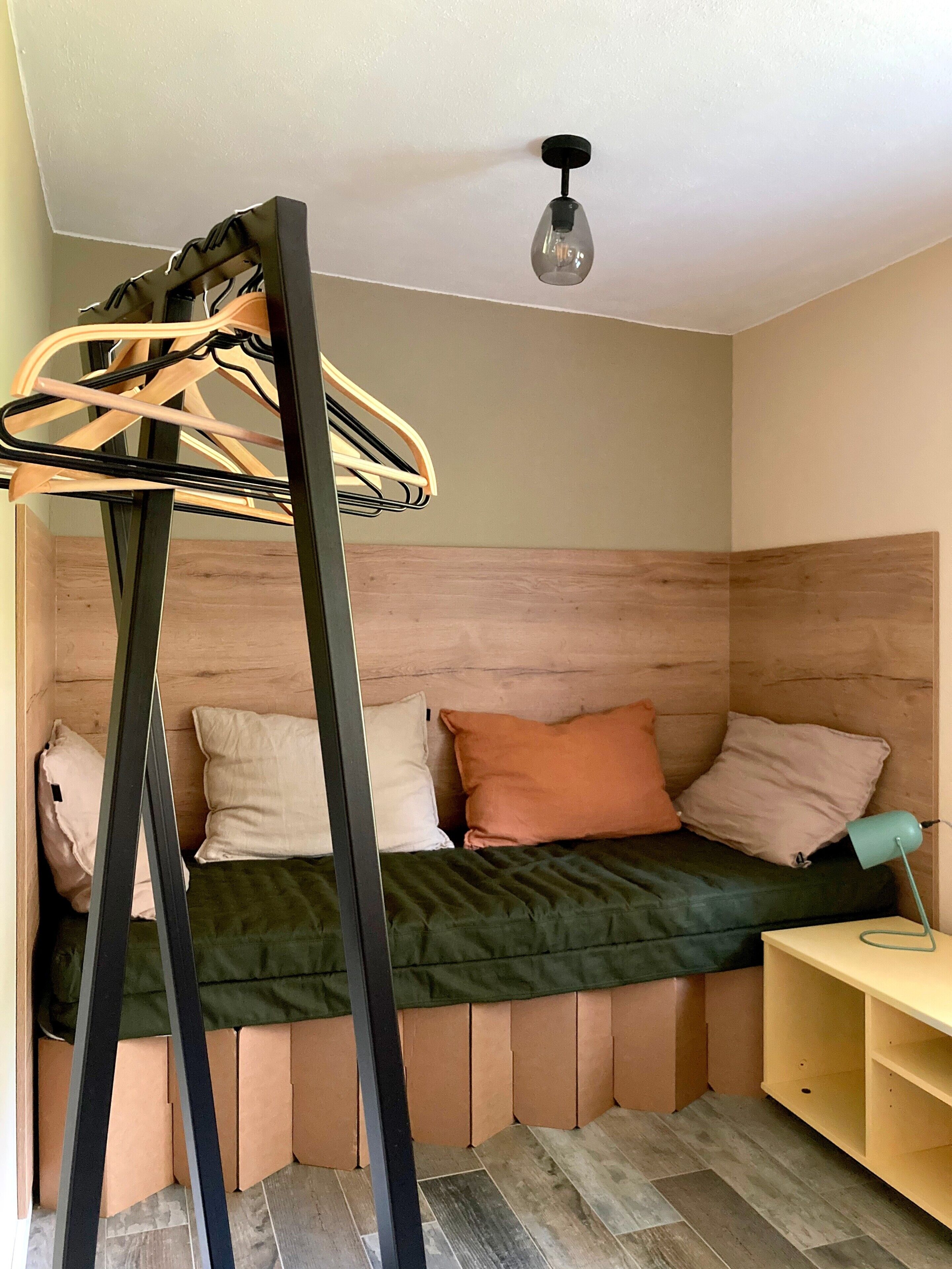 Een kamer met een bed, een houten hoofdbord, een hanglamp en een klein bureau met een lamp.