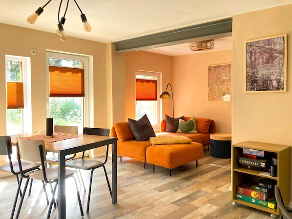 A modern living room with a sofa, a dining table with chairs, a bookshelf, and a painting on the wall.