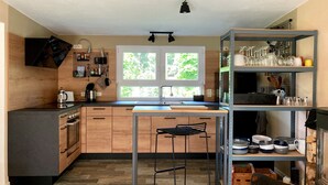 Une cuisine moderne avec des meubles en bois, un îlot central, un évier et une étagère en métal où sont rangés des verres.