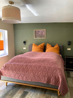 A bedroom with a bed, a hanging light fixture, a wall-mounted picture, and a window with blinds.
