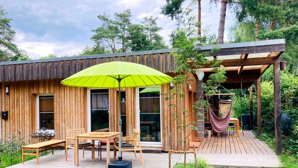 Une cabane en bois dotée d’une terrasse, de meubles de jardin et d’un hamac.