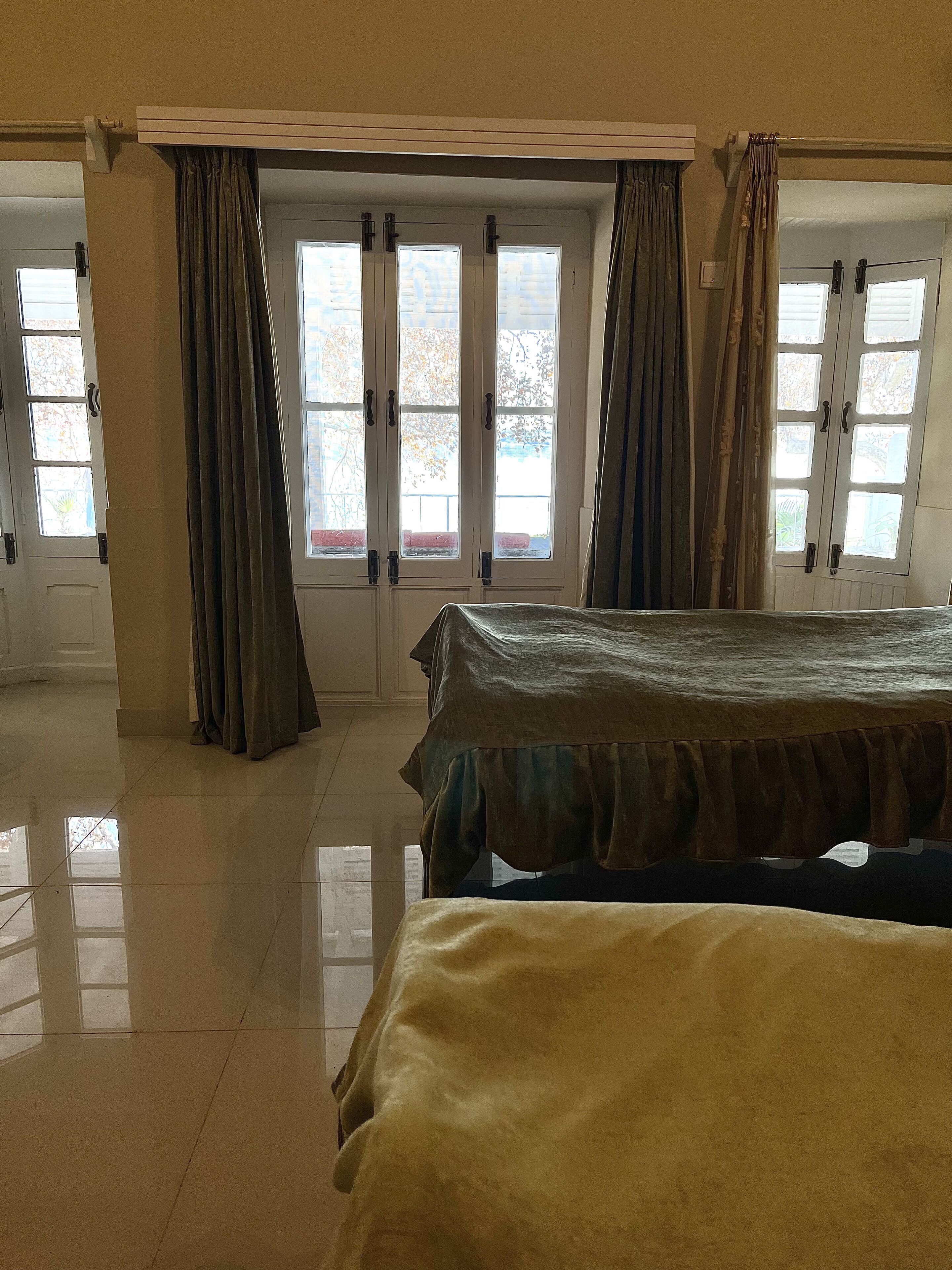 A hotel room with a bed, a large window with curtains, and a door with a handle.