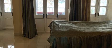 A hotel room with a bed, a large window with curtains, and a door with a handle.
