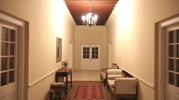 A hallway with a chandelier, a door at the end, and a small table with a vase.