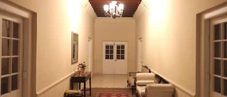 Un pasillo con un candelabro, una puerta al final y una pequeña mesa con un jarrón.