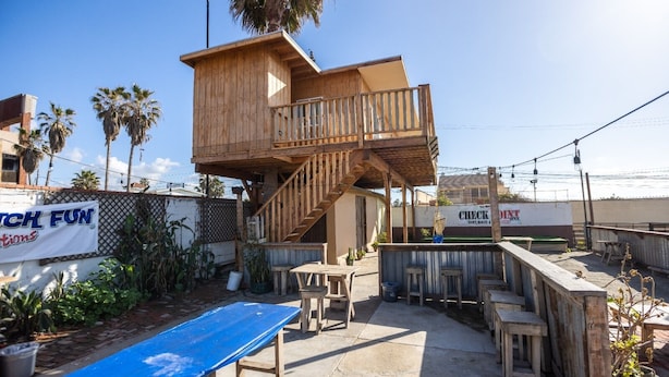A wooden deck with a staircase leading to a raised platform, surrounded by potted plants and outdoor furniture. - Rosarito Beach Rooms #1 (Rosarito)