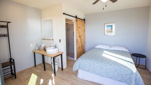 A bedroom with a bed, a bedside table with a sink, a shower area, and a ceiling fan. - Rosarito Beach Rooms #1 (Rosarito)