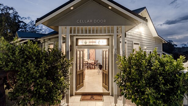 En väl upplyst entré med en skylt som visar texten ”Cellar Door”, ett matområde med stolar och en dörrmatta med en logotyp.