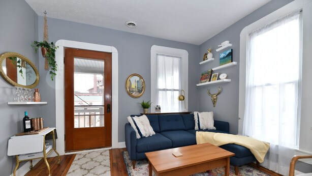Una sala de estar con un sofá azul, una mesa de centro de madera y una mesita auxiliar blanca con un espejo y adornos.
