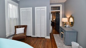 Un dormitorio con una cama, una silla, un aparador, un espejo y una puerta que da a otra habitación.
