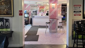 Een ijssalon met een roze en witte kleurstelling, een balie en twee krukken.