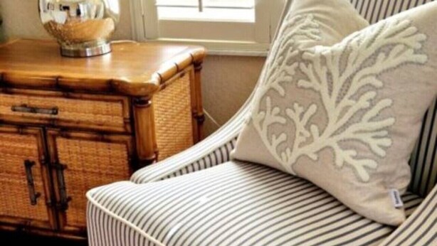 Een gestreepte fauteuil met een decoratief kussen, een houten dressoir en een lamp.
