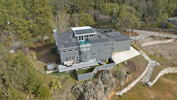 Uma casa moderna de dois andares, com painéis solares, um alpendre coberto e um muro de contenção de pedra.