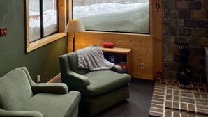 A cozy room with a large window, a fireplace, and a green armchair. - Sunrise Kirkwood Chalet with Red Cliffs View (Kirkwood)