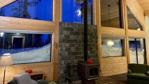 A high-ceilinged room with large windows, a stone fireplace, and a wooden interior. - Sunrise Kirkwood Chalet with Red Cliffs View (Kirkwood)
