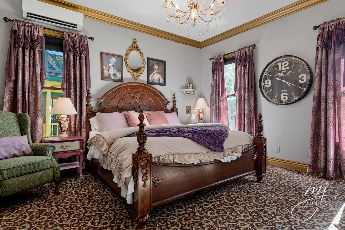 A classic bedroom with a wooden four-poster bed, a green armchair, and a patterned carpet.