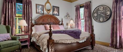 A classic bedroom with a wooden four-poster bed, a green armchair, and a patterned carpet.