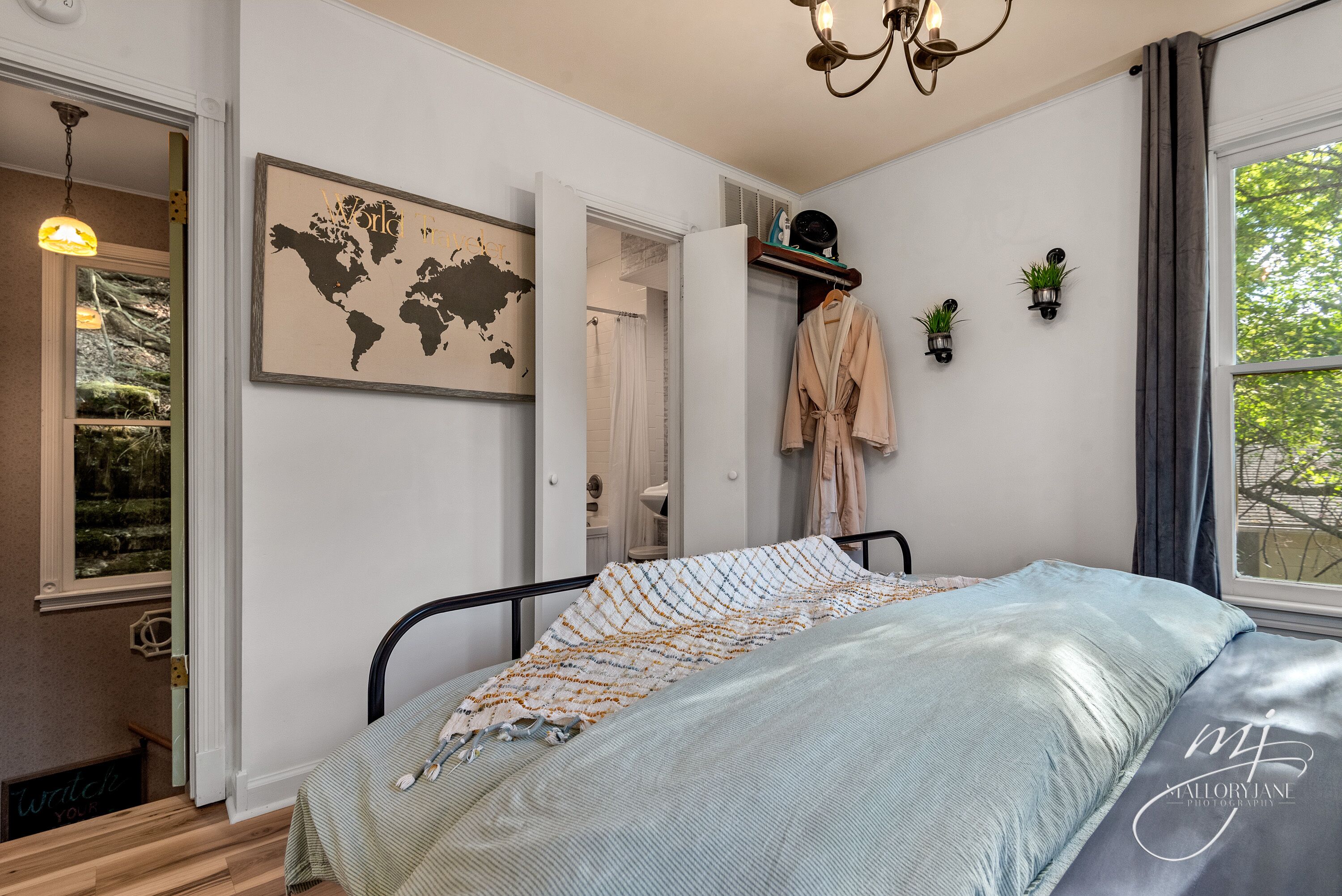 A bedroom with a bed, a world map on the wall, a robe hanging, and a window with curtains.
