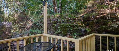 A wooden deck with a table and chairs, surrounded by a forested area.