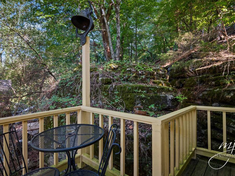 A wooden deck with a table and chairs, surrounded by a forested area.