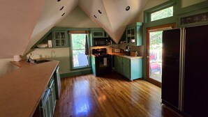 Una cocina con techo inclinado, piso de madera y armarios verdes.