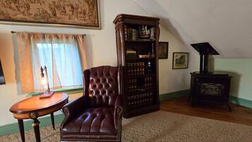 Una habitación con un sillón de cuero, una estantería de madera, una mesita con lámpara y un estufa de leña.