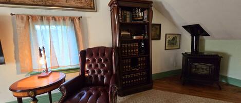 Una habitación con un sillón de cuero, una estantería de madera, una mesita con lámpara y un estufa de leña.