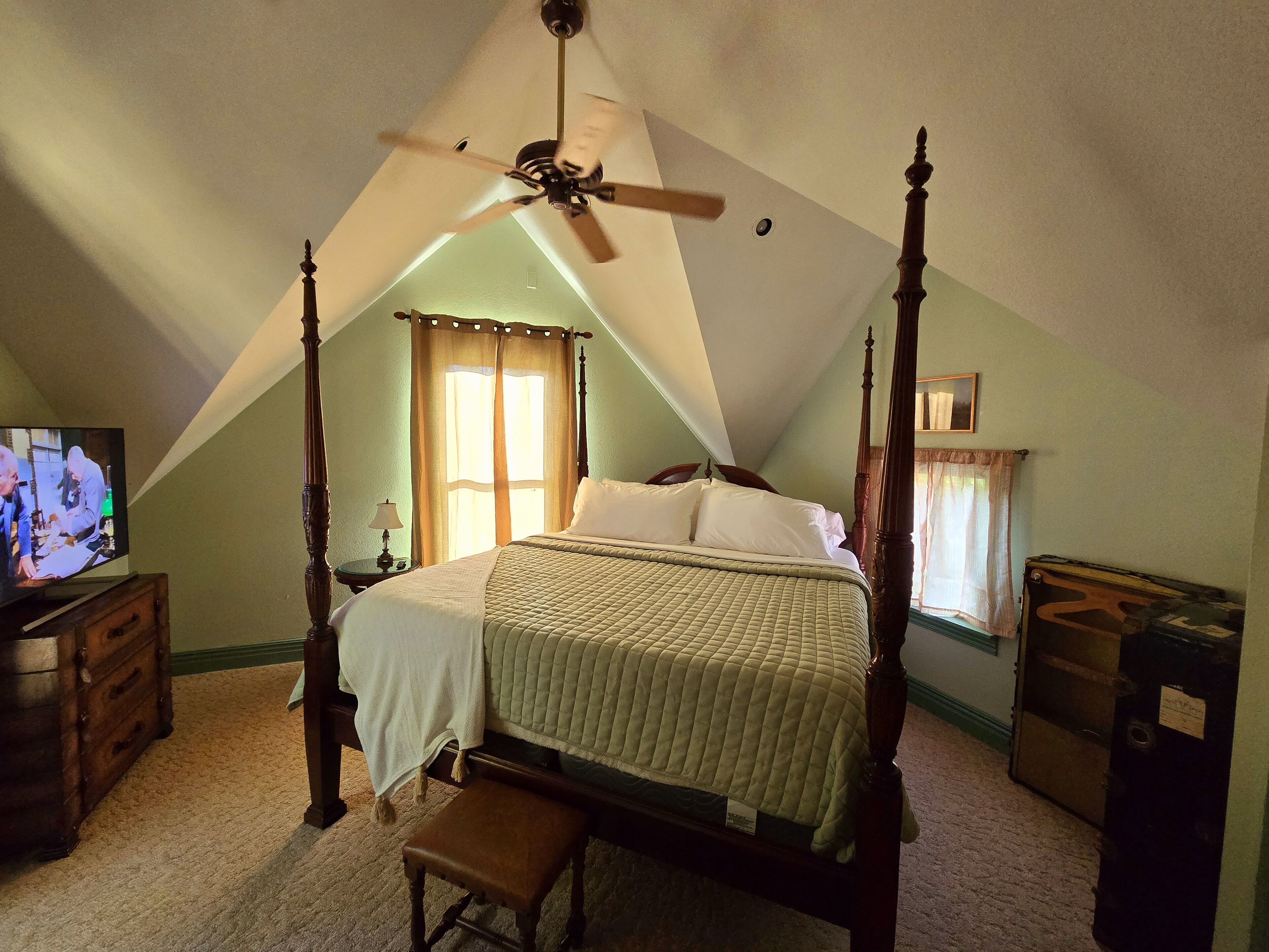 A bedroom with a four-poster bed, a ceiling fan, a television, and a dresser.