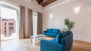 A spacious living room with a large window, a blue sofa, a white coffee table, and a potted plant. - Luisa Apartment (Cagliari)
