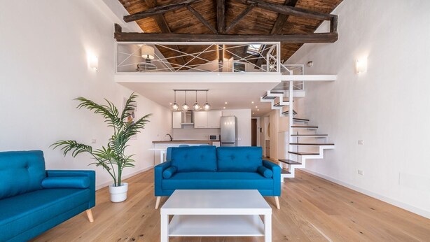 A spacious living area with a high ceiling, a staircase, and a kitchen in the background. - Luisa Apartment (Cagliari)