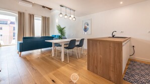 A modern living room with a sofa, dining table, chairs, and a small kitchen area. - Luisa Apartment (Cagliari)