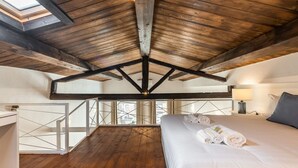 A bedroom with a wooden ceiling, a bed with rolled towels, a nightstand, and a window overlooking a cityscape. - Luisa Apartment (Cagliari)