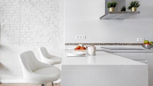 Una cucina moderna con mobili bianchi, una parete in mattoni bianchi, una cappa in acciaio inossidabile e un design minimalista.
