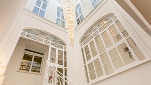 Een statig atrium met hoge plafonds, brede bogenramen en een centraal hanglamp.