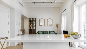 Een moderne keuken met een centraal eiland, een eethoek met een witte tafel en stoelen, en een zithoek met een bank en decoratieve spiegels.