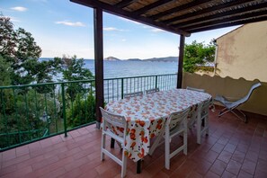 Una terraza con mesa y sillas, con vista a un cuerpo de agua y colinas.