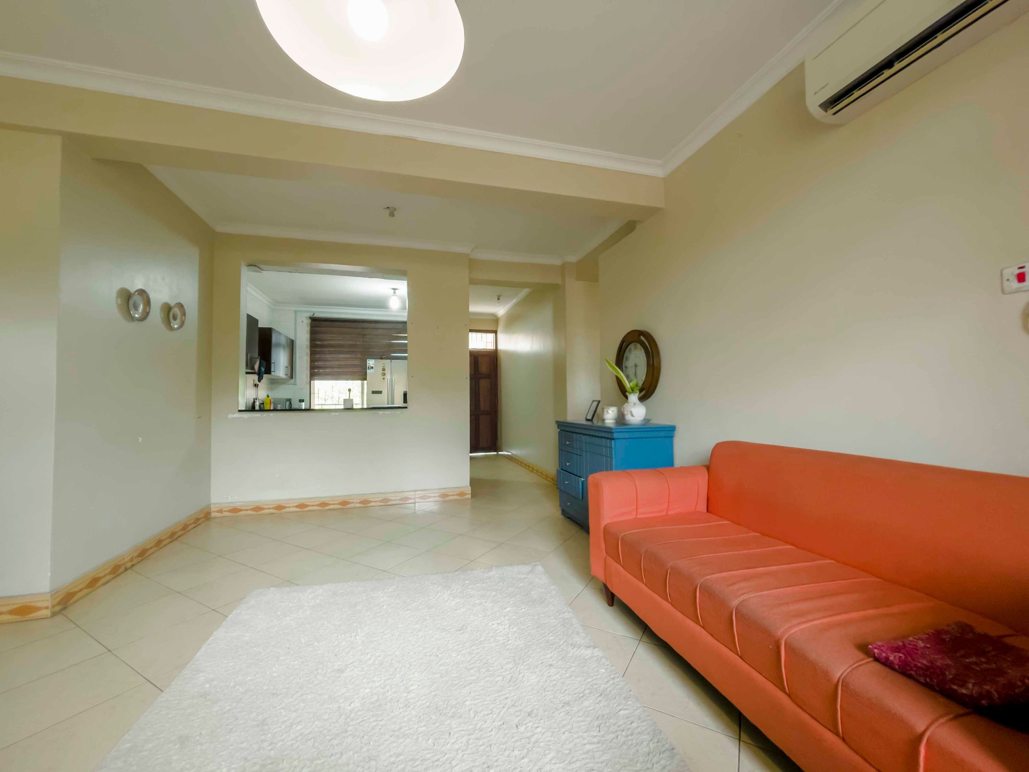 A living room with a white rug, orange sofa, and a blue cabinet.