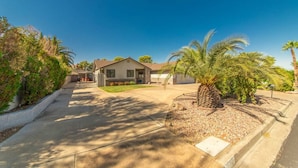 A single-story house with a front yard, a palm tree, and a clear blue sky. - Calcutta · Relax in Style!! Pool, Vegas games, RV Parking (Henderson)