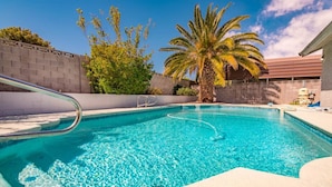 A clear blue pool with a metal ladder, surrounded by a concrete wall and palm trees. - Calcutta · Relax in Style!! Pool, Vegas games, RV Parking (Henderson)