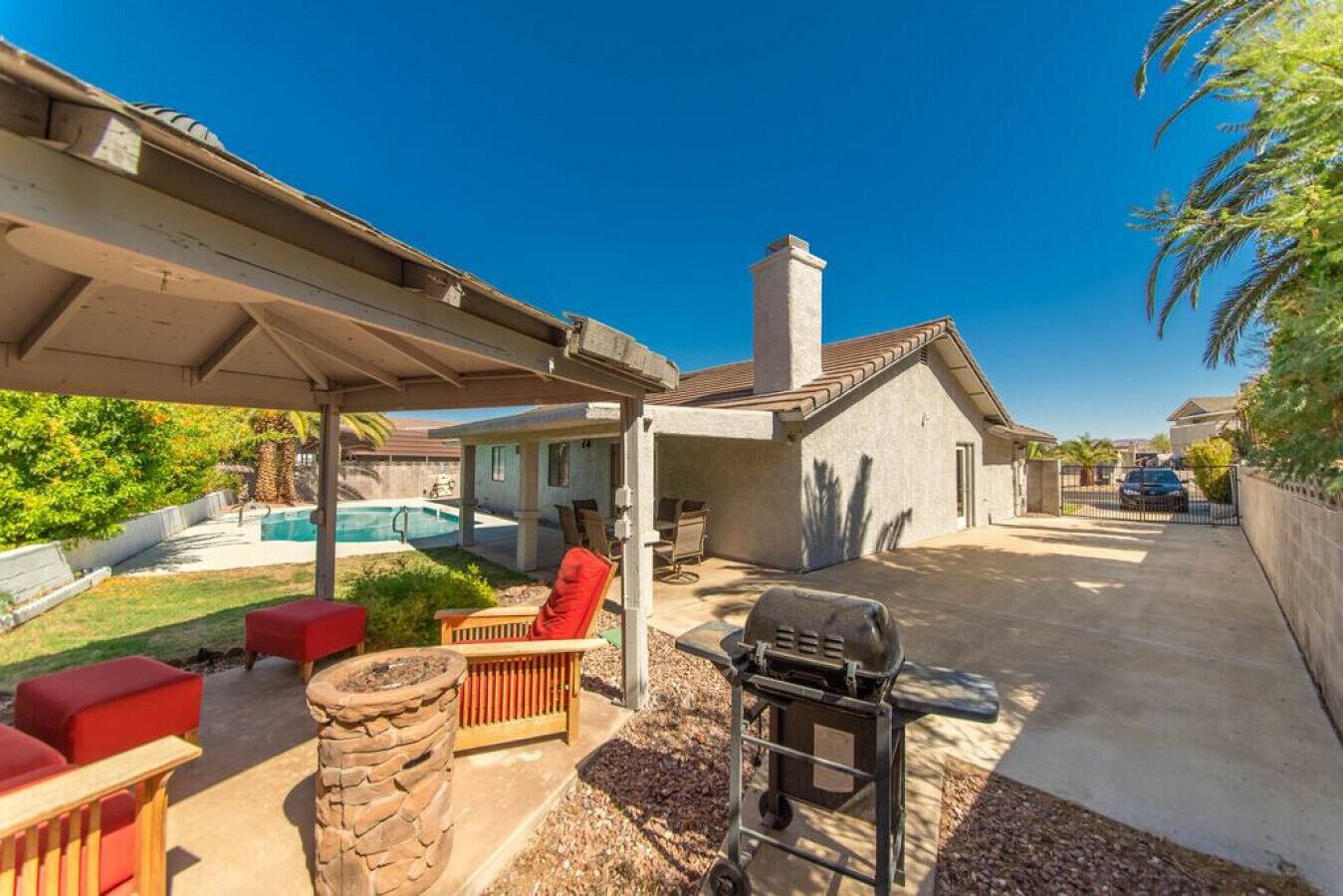 Une terrasse couverte avec des sièges d’extérieur, un barbecue et une piscine en arrière-plan.