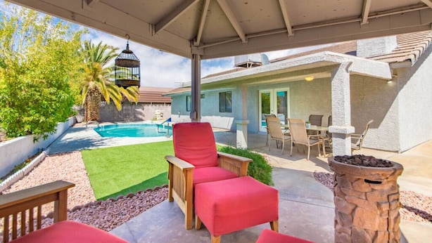 A covered patio with a pool, red chairs, and a stone fire pit. - Calcutta · Relax in Style!! Pool, Vegas games, RV Parking (Henderson)