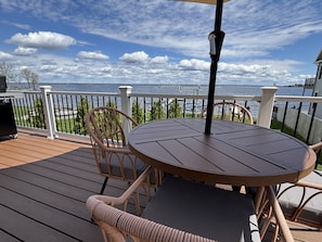 Une terrasse avec une table ronde et des chaises en osier, donnant sur une étendue d’eau.
