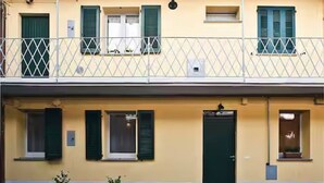Un edificio de dos pisos con un balcón, ventanas con contraventanas y una puerta.